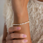 A hand with light pink nails wears the Vertical Baguette Tennis Bracelet—a gold piece set with rectangular white stones that resemble baguette diamonds.