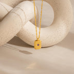 Ribbed Birthstone Star Necklace with a purple stone, showcased against a textured, curved, off-white sculpture.