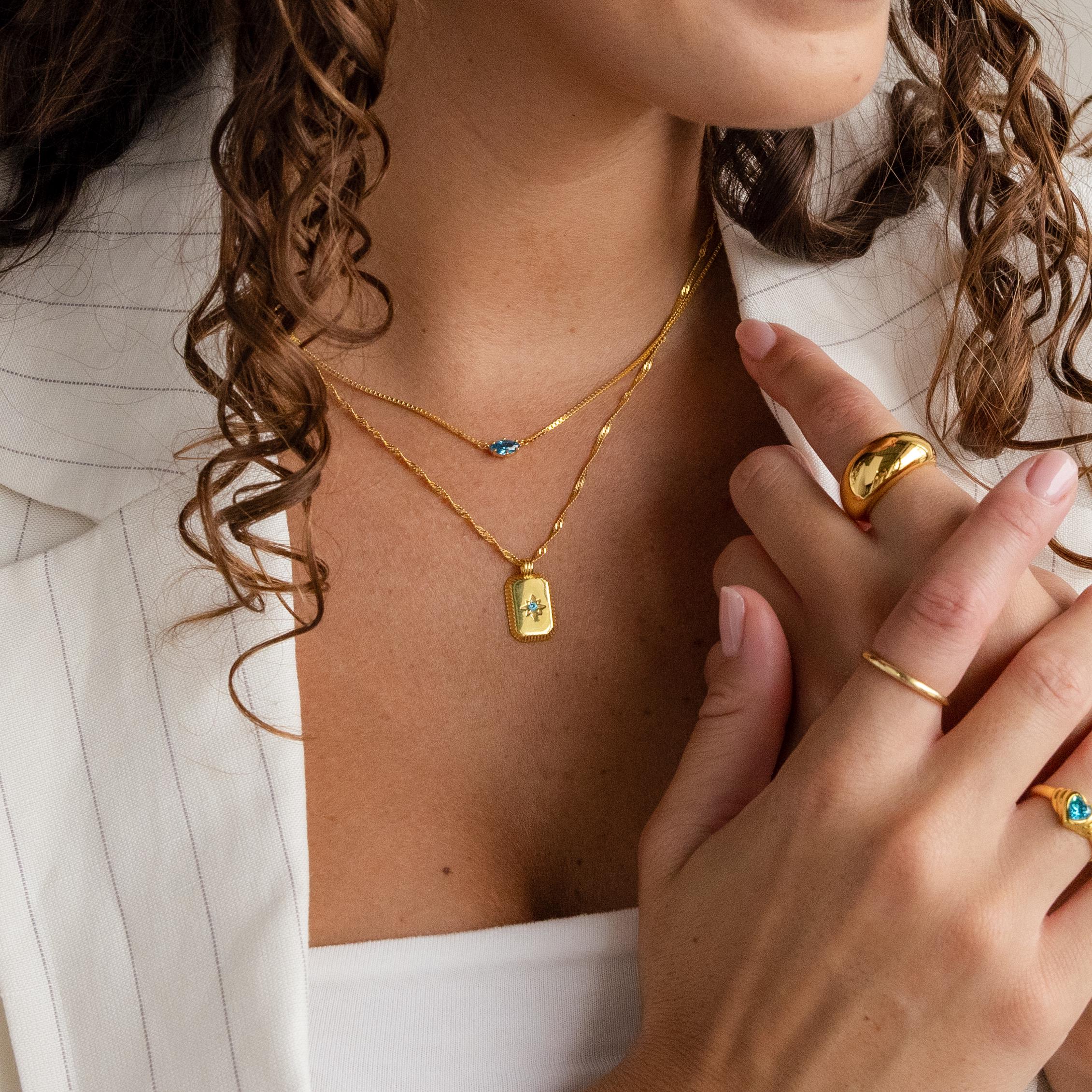 Woman with curly hair wears a white pinstripe blazer, gold rings, and the Ribbed Birthstone Star Necklace layered with other gold necklaces.