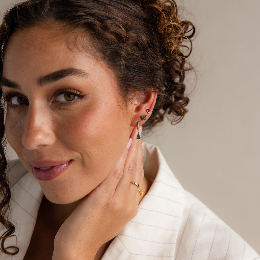 Woman with curly hair wears Butterfly Birthstone Studs, touches her face, and smiles softly at the camera.