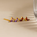 Marquise Petal Birthstone Studs in gold showcase two marquise gemstones—one pair purple, one red—displayed on a beige surface. These elegant studs are perfect as personalized birthstone jewelry.
