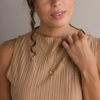 Woman in a beige pleated sleeveless top touches her Evil Eye Birthstone Hand Necklace.