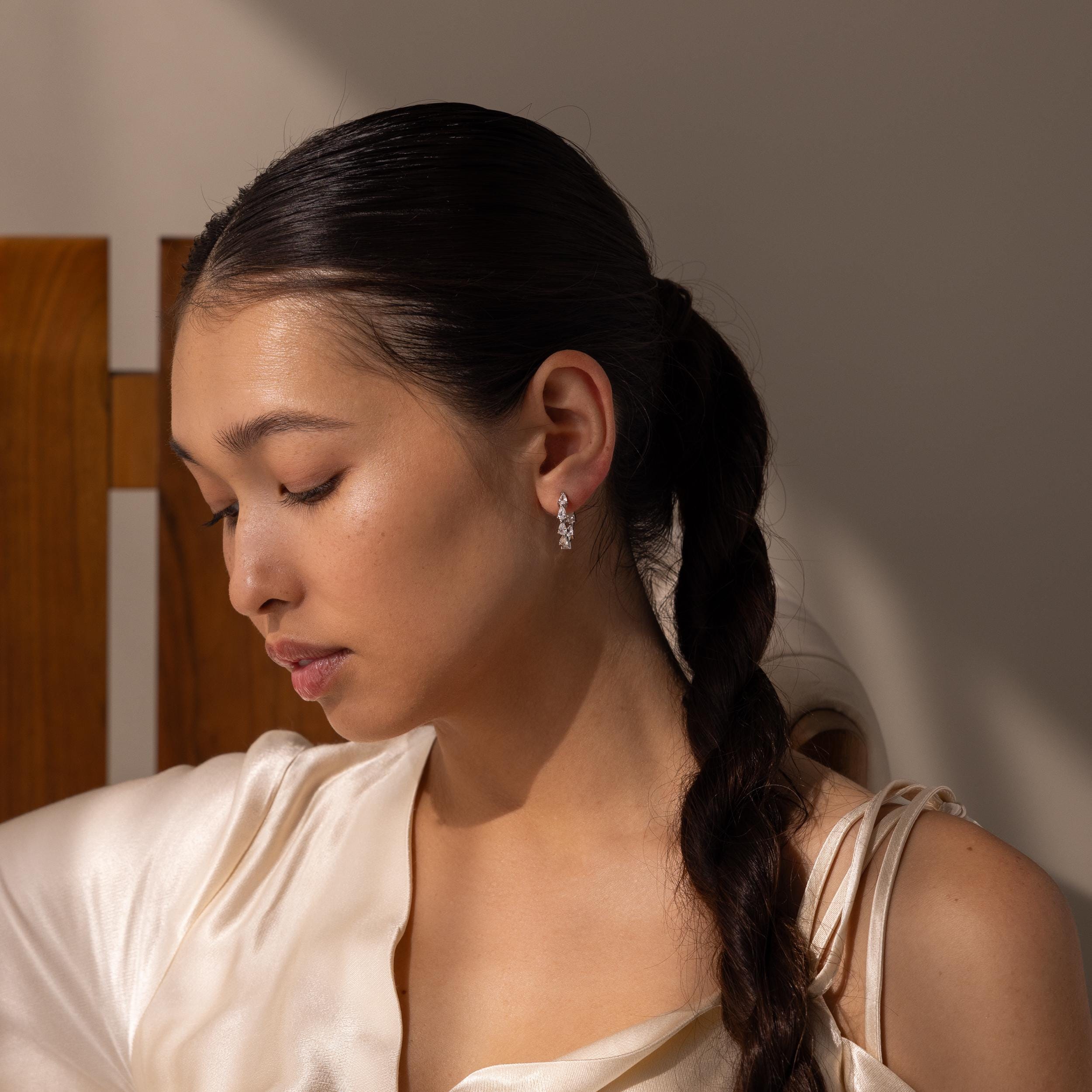 Woman with long braid and pearl earrings, in a silk top under soft lighting—an elegant look that’s perfect for gifting or pairing with the Inside Out Pear Diamond Hoops.