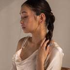 A woman wearing Duo Pave Link Hoops and a satin dress gently holds her braided hair, gazing downward under soft lighting.