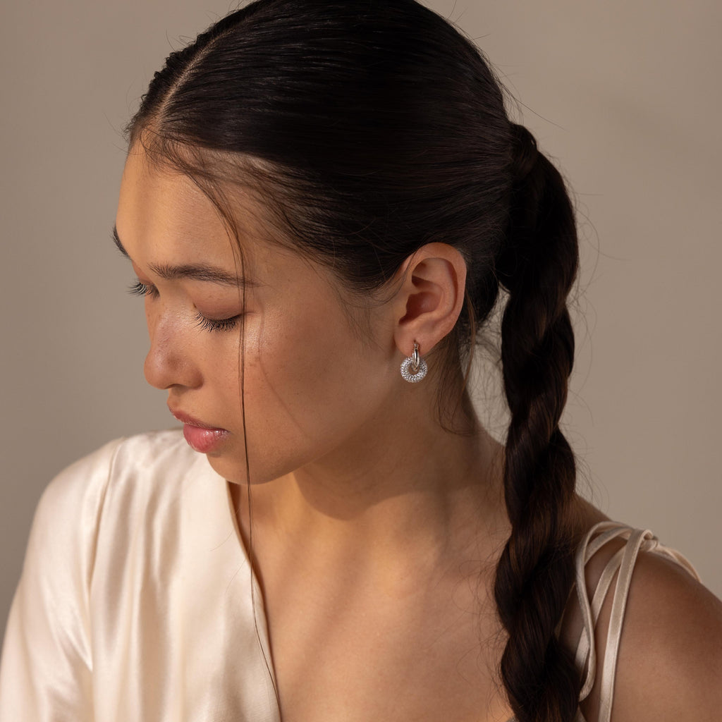 A woman with braided hair in a cream satin top looks down, showcasing the Duo Pave Link Hoops for a touch of modern elegance.