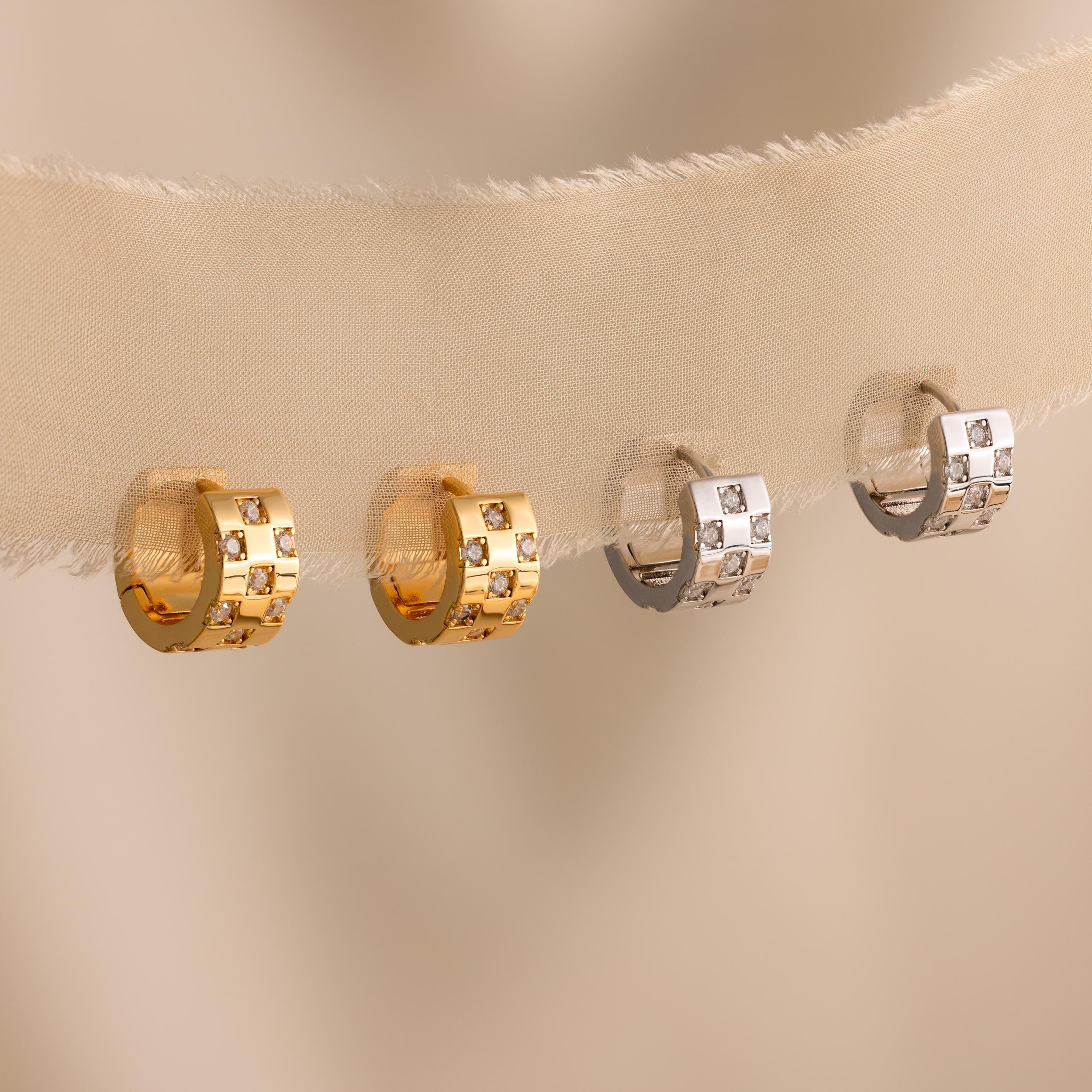 Two gold and two silver Pave Checkered Huggies, each set with square engravings and small gemstones, hang elegantly on fabric.