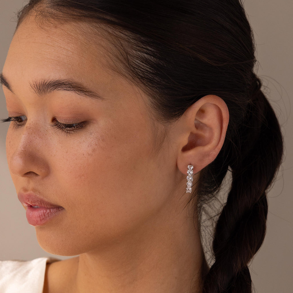 Woman with braided hair wearing Inside Out Heart Diamond Hoops, featuring multiple sparkling diamonds, looking down with a neutral expression.