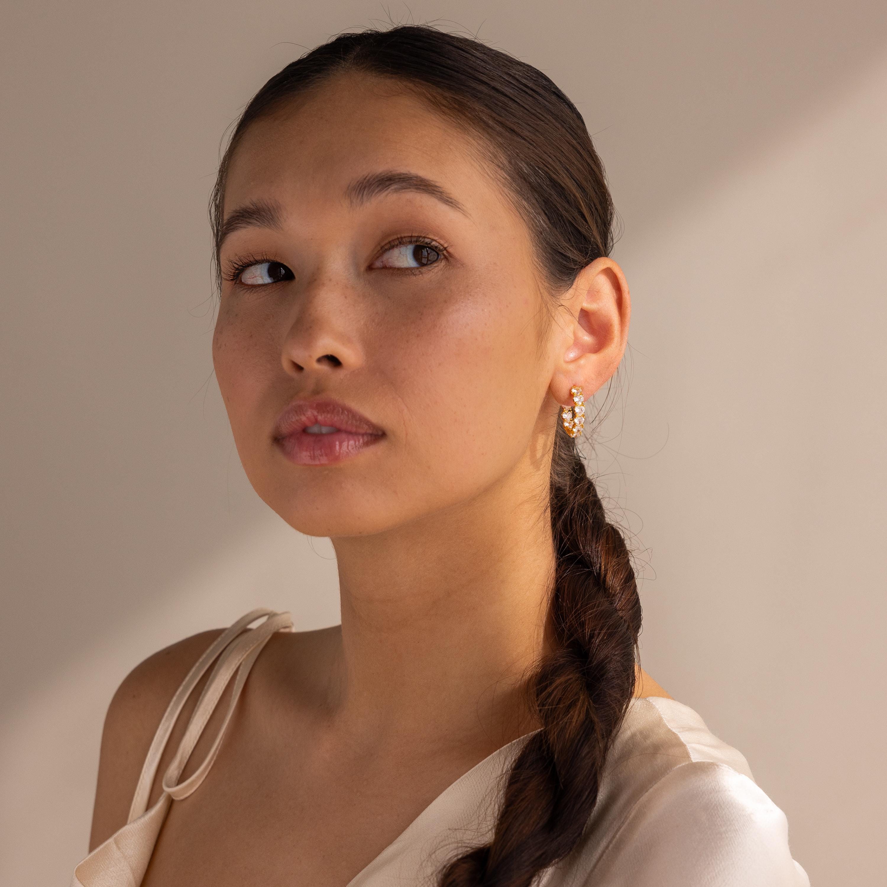 Woman with a long dark braid, wearing Inside Out Heart Diamond Hoops and a cream satin top, gazes slightly upward.