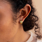 Close-up of a person wearing the Pave Checkered Huggies—gold hoop earrings embellished with small pave gemstones.