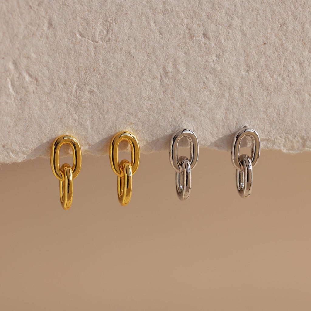 Two pairs of Link Drop Studs, one in gold and one in silver, elegantly displayed on a textured beige surface—perfect earrings for any occasion.