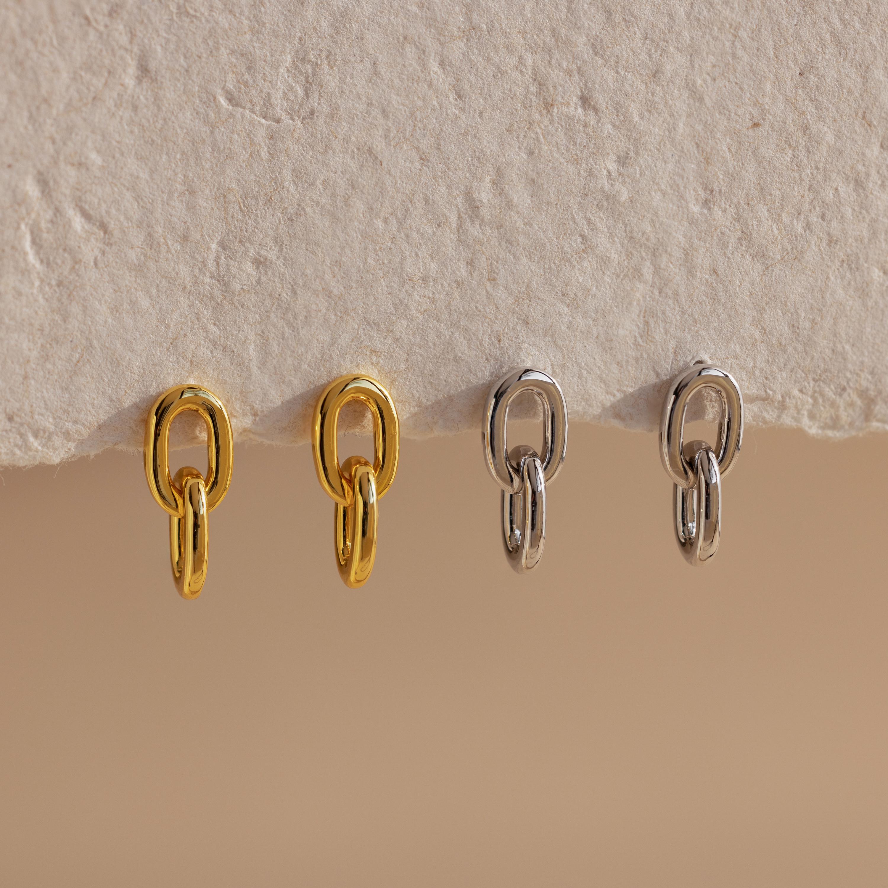 Two pairs of Link Drop Studs, one in gold and one in silver, elegantly displayed on a textured beige surface—perfect earrings for any occasion.
