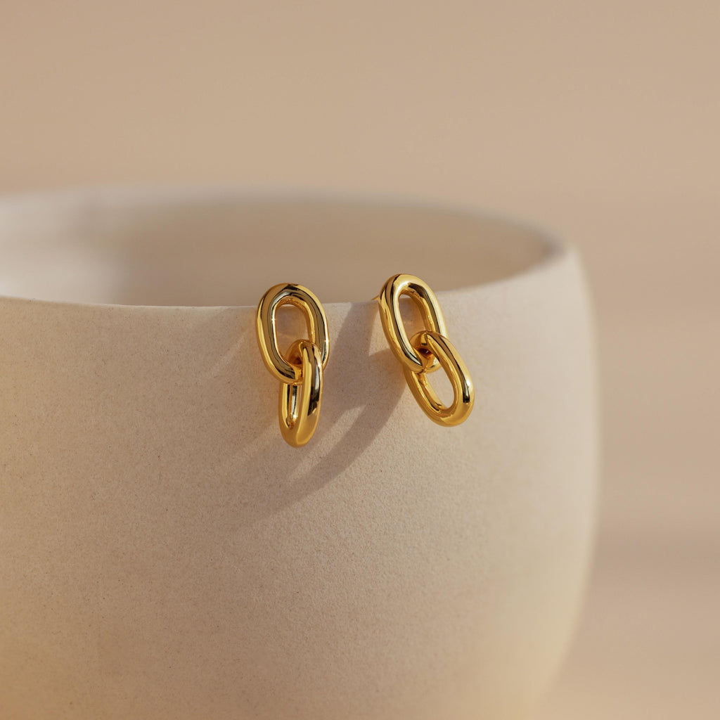Link Drop Studs hang on the edge of a smooth, light beige ceramic cup against a gentle background—stylish earrings perfect for any occasion.