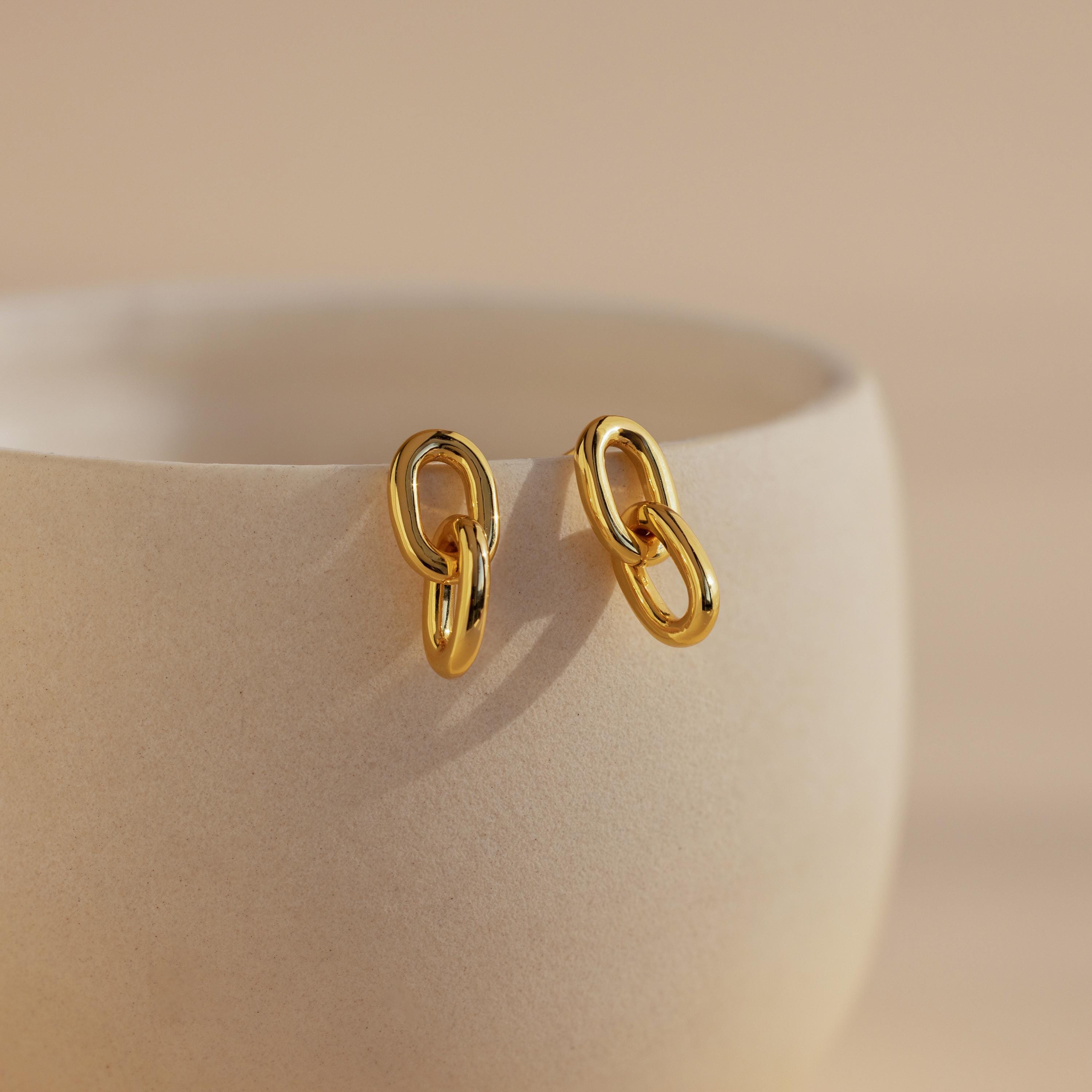 Link Drop Studs hang on the edge of a smooth, light beige ceramic cup against a gentle background—stylish earrings perfect for any occasion.