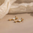 The Opal & Diamond Drop Studs, featuring opal and sparkling diamonds, rest on a beige surface beside a soft fabric—perfect dainty earrings for any occasion.