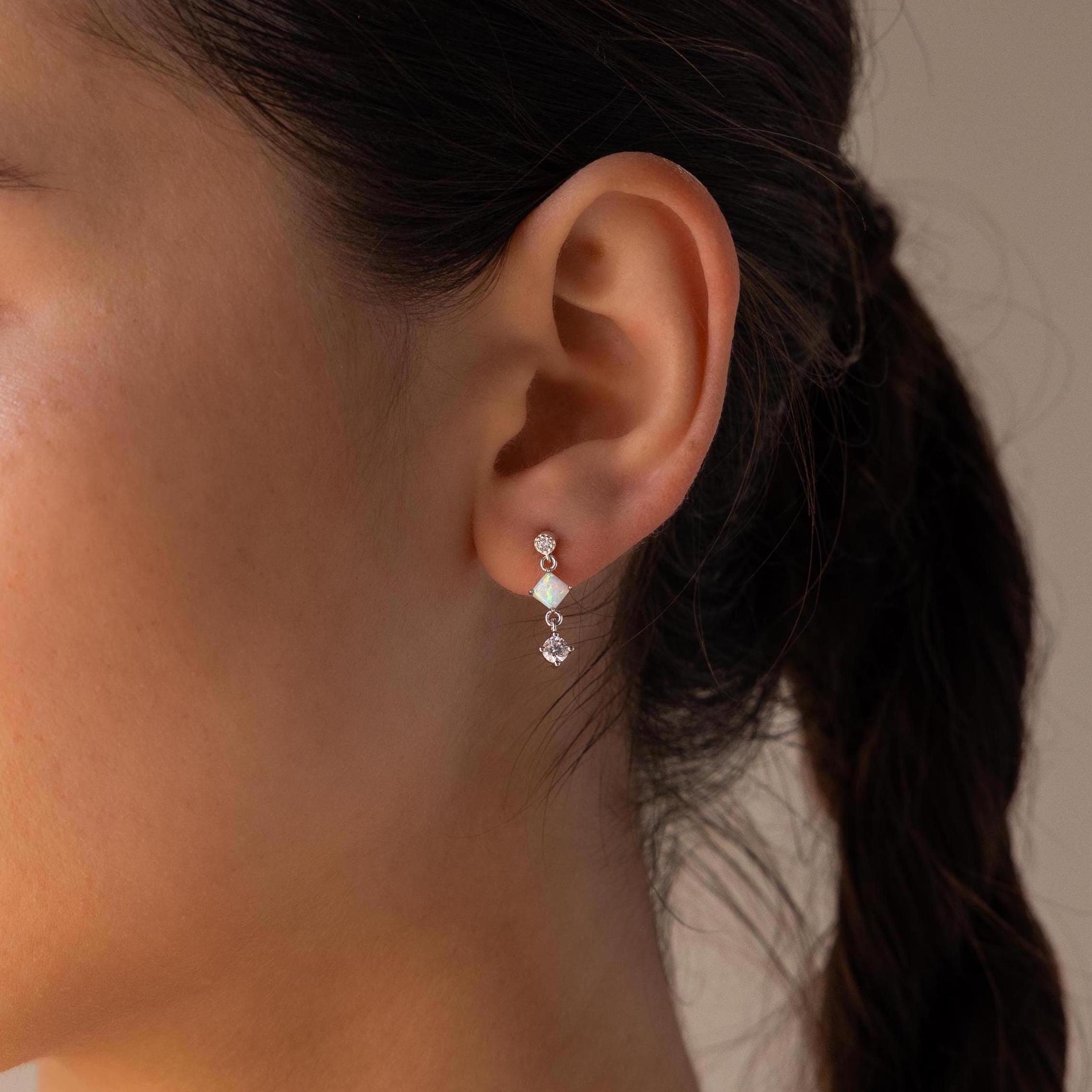 Close-up of a woman's ear wearing the Opal & Diamond Drop Studs, featuring dainty earrings with two crystals and a floral stud design for an elegant look.