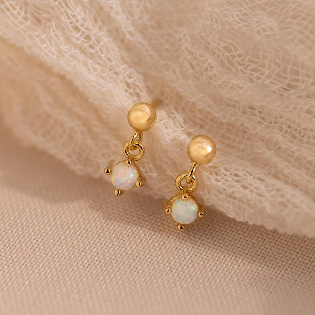 Dainty Opal Drop Studs with small sparkling opals rest on a soft beige fabric—lightweight and perfect for everyday wear. Add an elegant touch to any look with these dainty earrings.