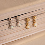 Two pairs of Dainty Opal Drop Studs—one silver and one gold—are elegantly displayed on a closed book, showcasing their lightweight design and adding a touch of sophistication.