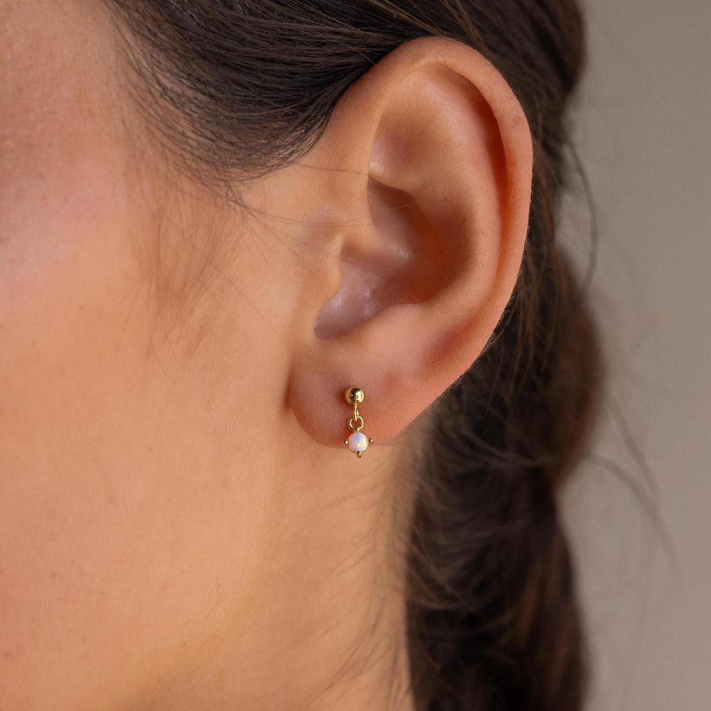 Close-up of a woman's ear wearing Dainty Opal Drop Studs—elegant gold studs featuring a delicate opal drop, perfect for those who love lightweight, dainty earrings.