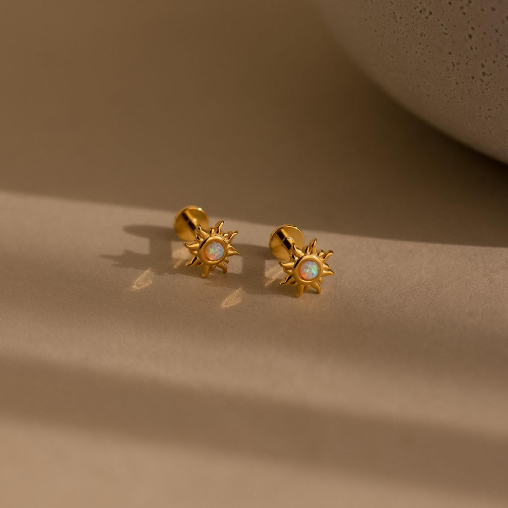 Opal Sun Flat Back Studs feature a central opal stone in a celestial design, resting elegantly on a beige surface under soft lighting. These flat back earrings combine comfort and radiance, perfect for any look.
