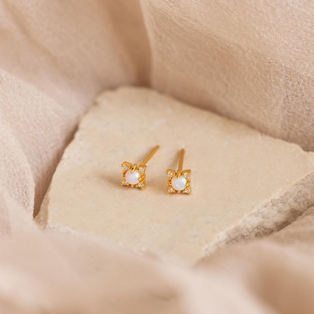 Opal Diamond Star Studs featuring small opals rest on a light beige stone surface, ideal for adding celestial elegance.
