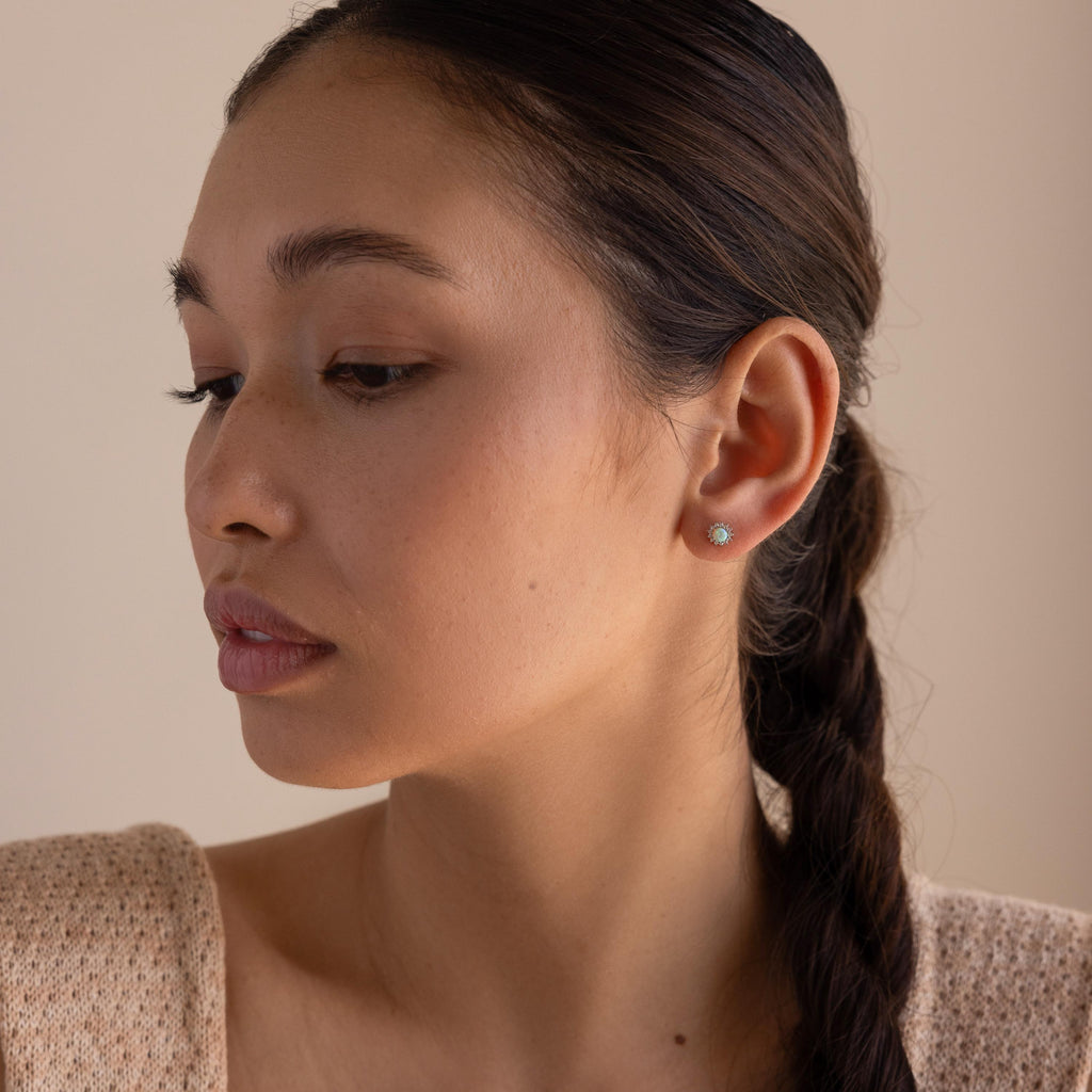Woman with braided hair wears Pave Opal Moon Studs and a beige textured top, the celestial earrings adding a subtle shimmer against the neutral backdrop.