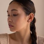 Woman with braided hair wears Pave Opal Moon Studs and a beige textured top, the celestial earrings adding a subtle shimmer against the neutral backdrop.