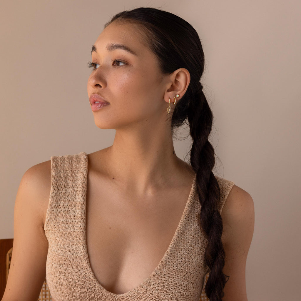 A woman with a long dark braid, in a beige sleeveless top, looks to the side against a neutral background while wearing Pave Opal Moon Studs.