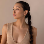 A woman with a long dark braid, in a beige sleeveless top, looks to the side against a neutral background while wearing Pave Opal Moon Studs.