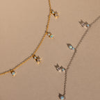 The Opal Diamond Station Necklace set features delicate gold and silver chains with crystal and opal charms, making a perfect bridesmaid keepsake, beautifully displayed on a beige surface.