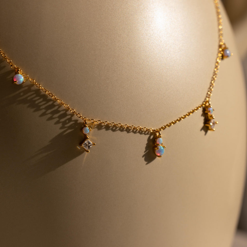 The Opal Diamond Station Necklace features small opal and star-shaped charms, making it an ideal birthstone gift or bridesmaid keepsake, shown on a beige background.