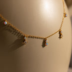 The Opal Diamond Station Necklace features small opal and star-shaped charms, making it an ideal birthstone gift or bridesmaid keepsake, shown on a beige background.