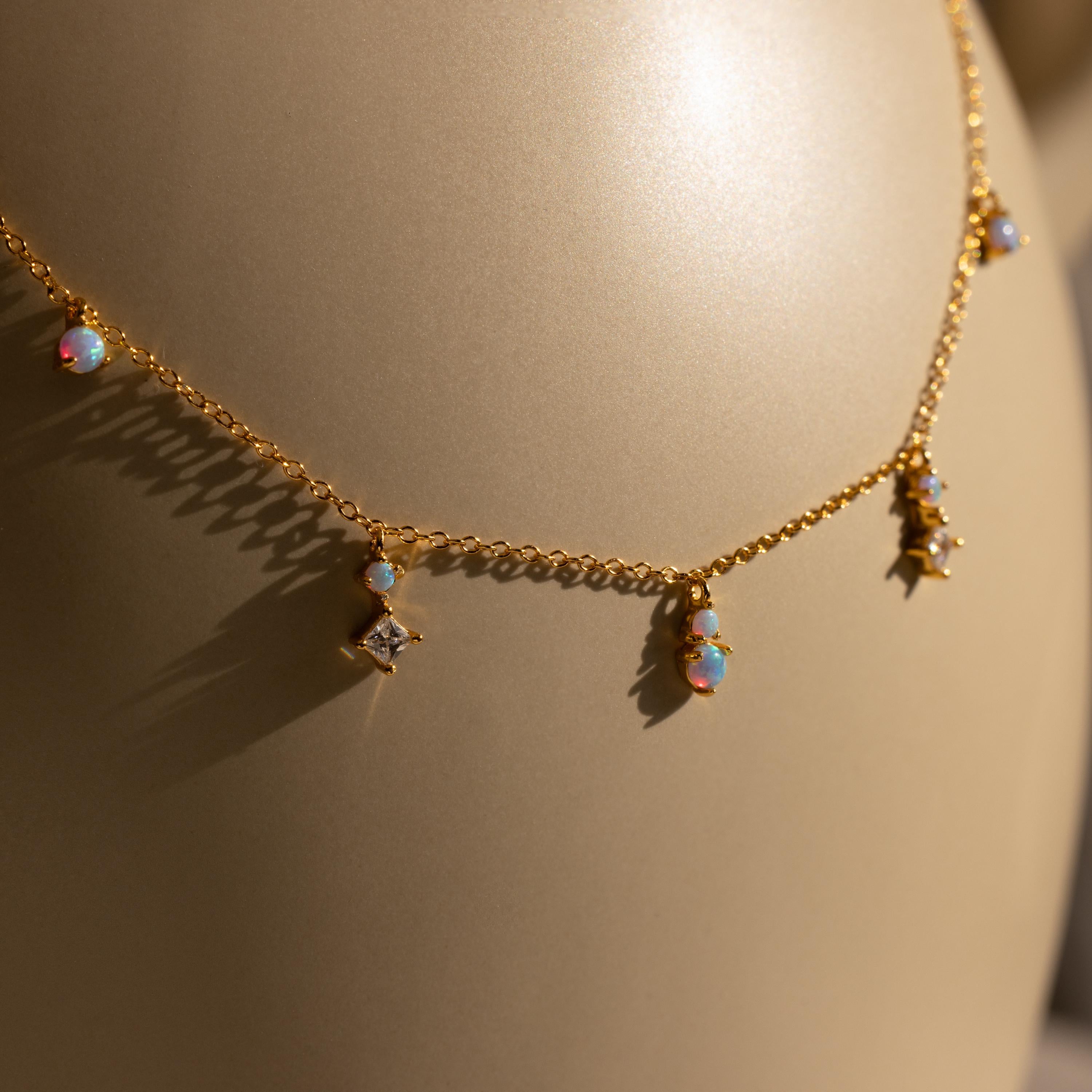 The Opal Diamond Station Necklace features small opal and star-shaped charms, making it an ideal birthstone gift or bridesmaid keepsake, shown on a beige background.