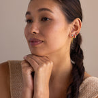 Woman with braided hair rests her chin on her hands, wearing Blue Opal Beaded Huggies and a sleeveless beige top.