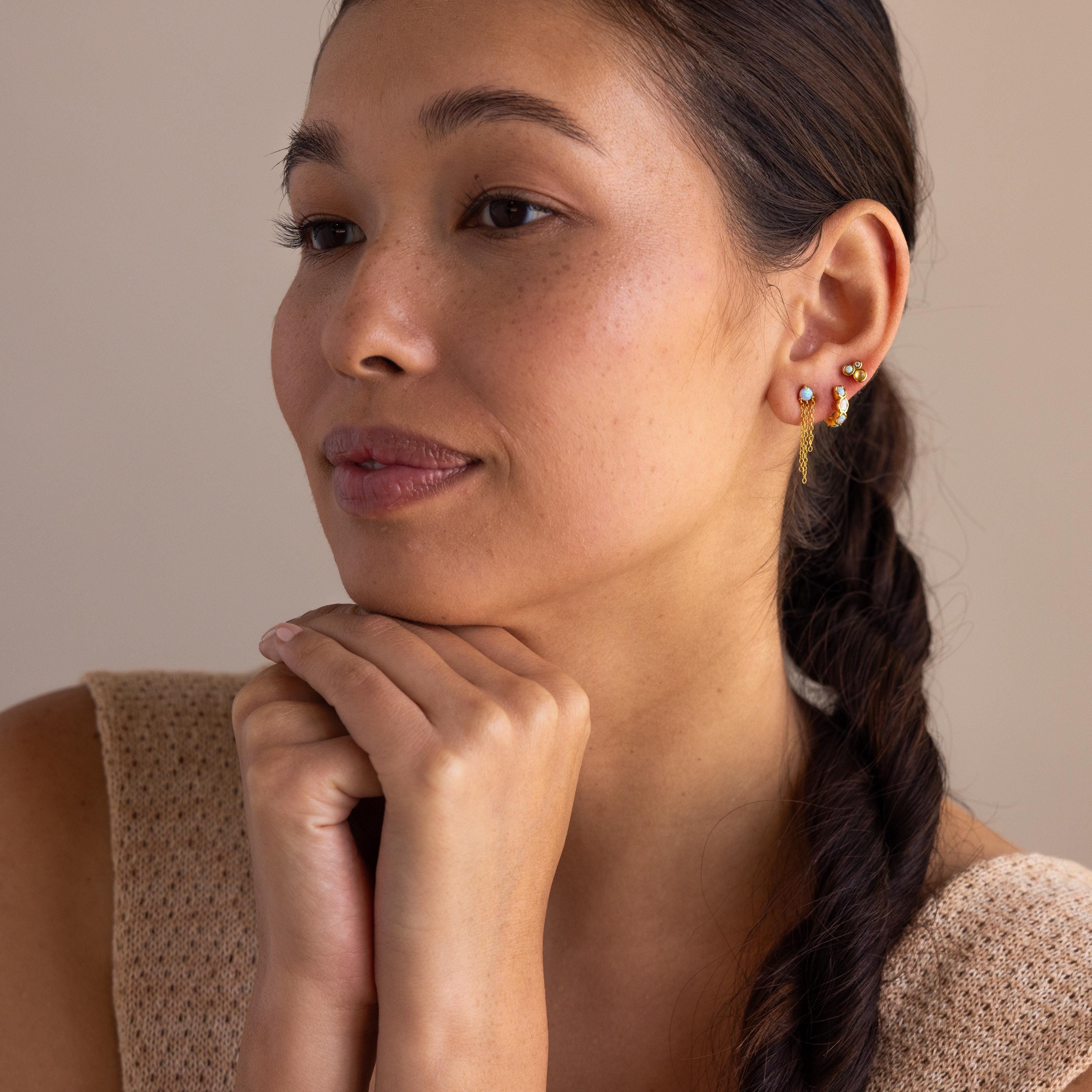 Woman with braided hair rests her chin on her hands, wearing Blue Opal Beaded Huggies and a sleeveless beige top.