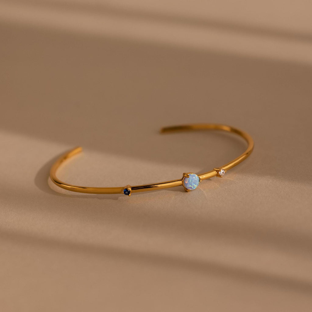 Minimalist Opal & Diamond Cuff Bracelet featuring elegant gemstones, showcased on a neutral beige surface with soft shadows.