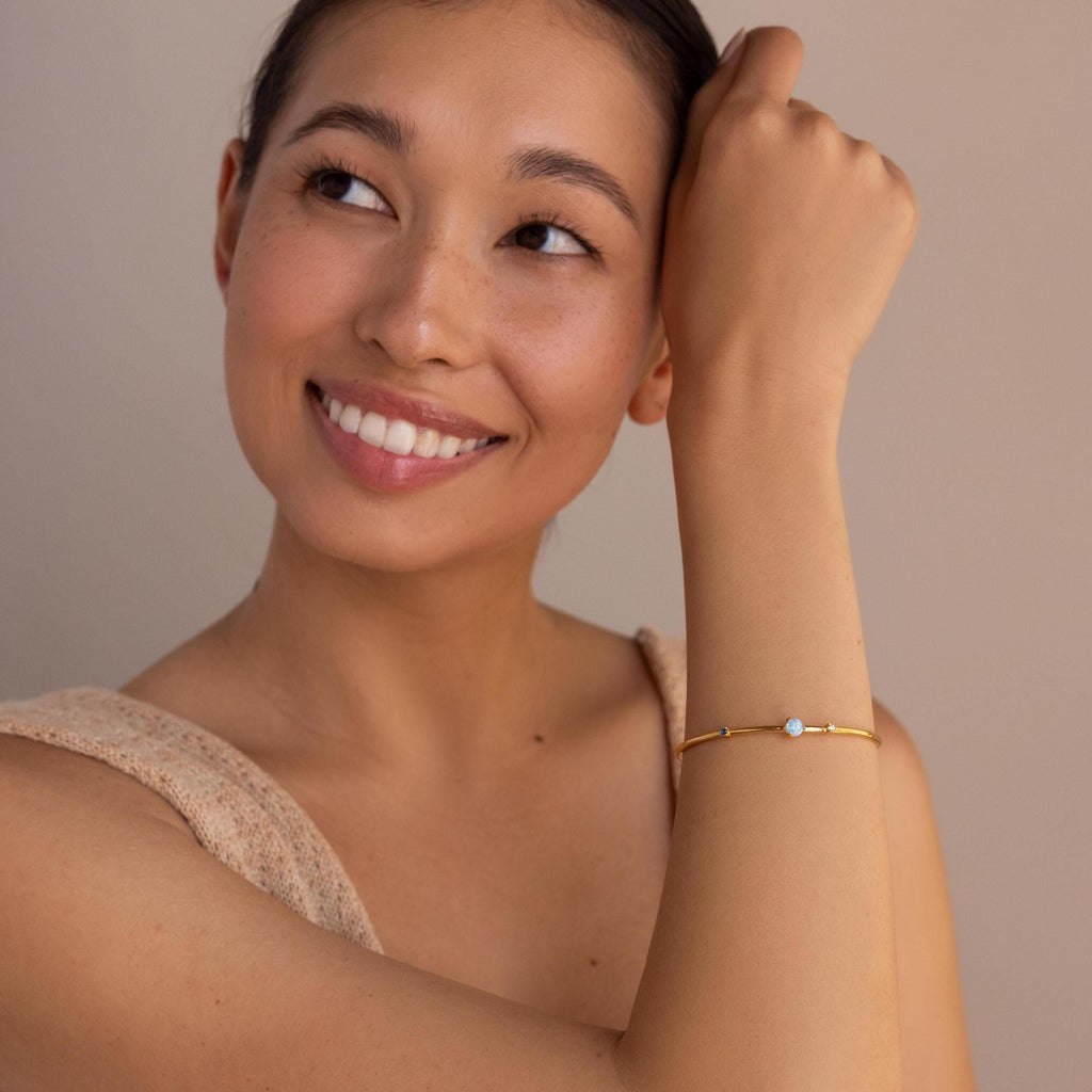 A woman smiles and looks up, wearing the Opal & Diamond Cuff Bracelet with a delicate opal and diamond accent, set against a neutral background.
