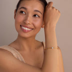 A woman smiles and looks up, wearing the Opal & Diamond Cuff Bracelet with a delicate opal and diamond accent, set against a neutral background.