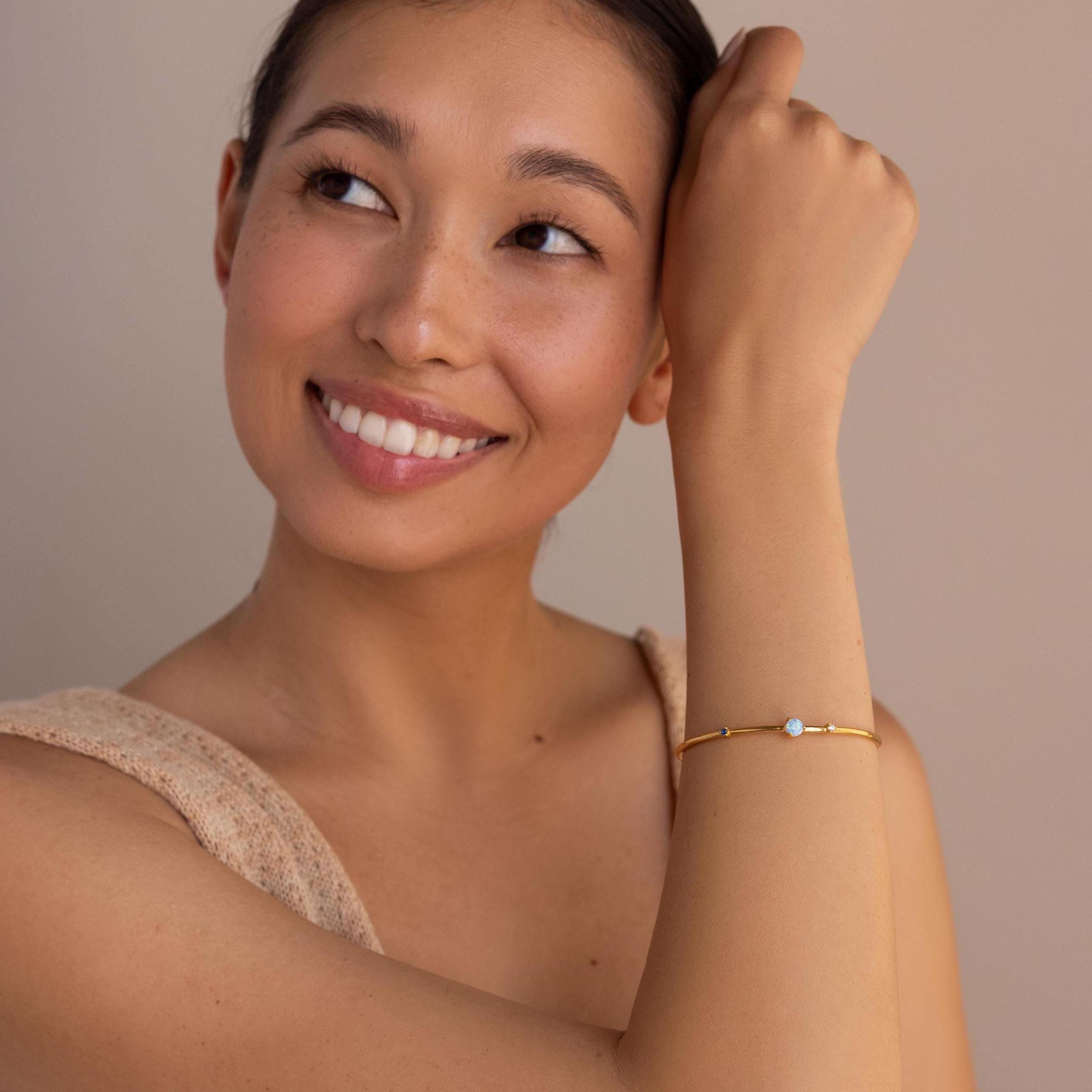 A woman smiles and looks up, wearing the Opal & Diamond Cuff Bracelet with a delicate opal and diamond accent, set against a neutral background.