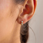 Close-up of an ear wearing the Blue Opal Beaded Huggies, a small gold hoop earring adorned with two light blue opal beads.