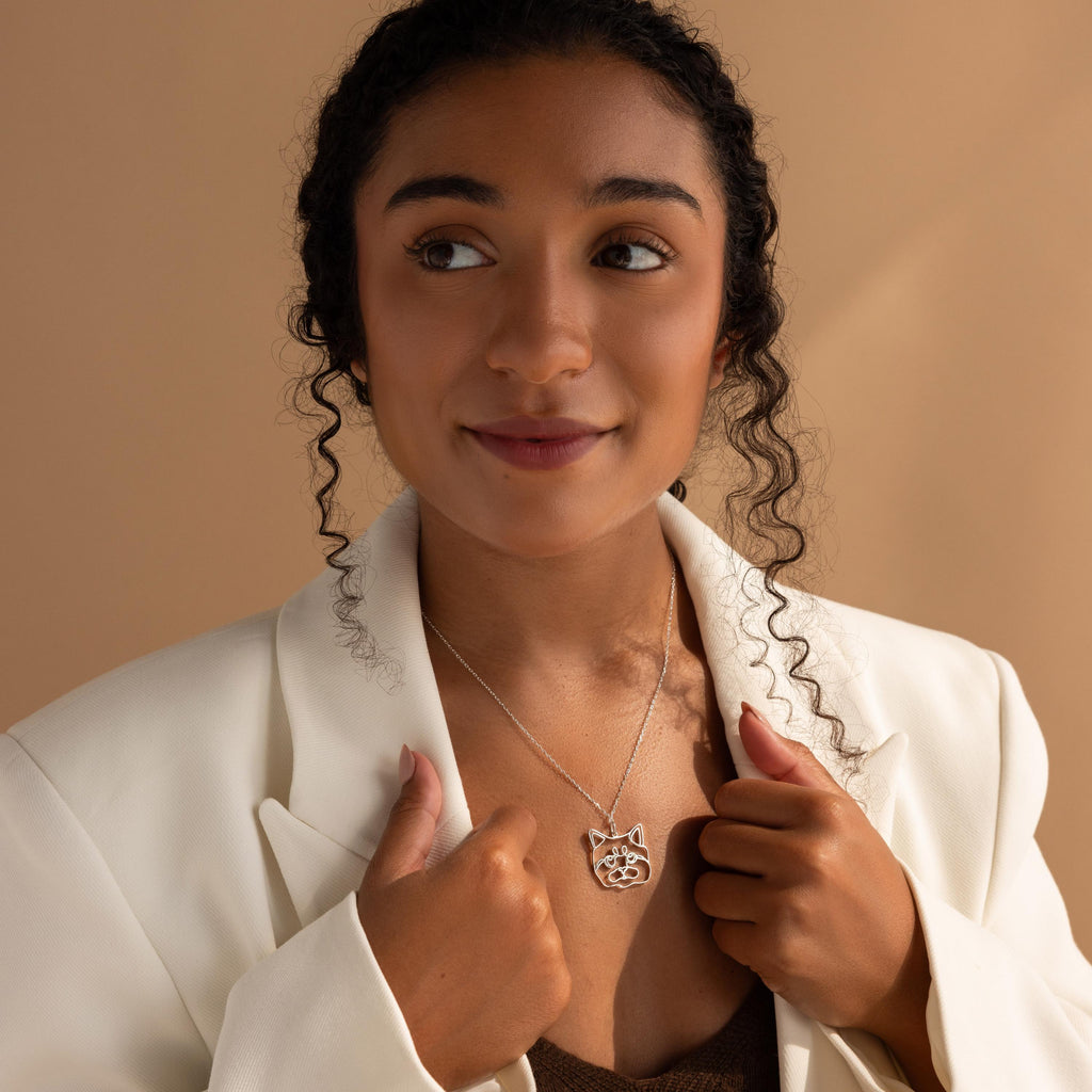 Woman in a white blazer holding a Custom Pet Line Art Necklace shaped like a cat, looking slightly to the side against a neutral background.