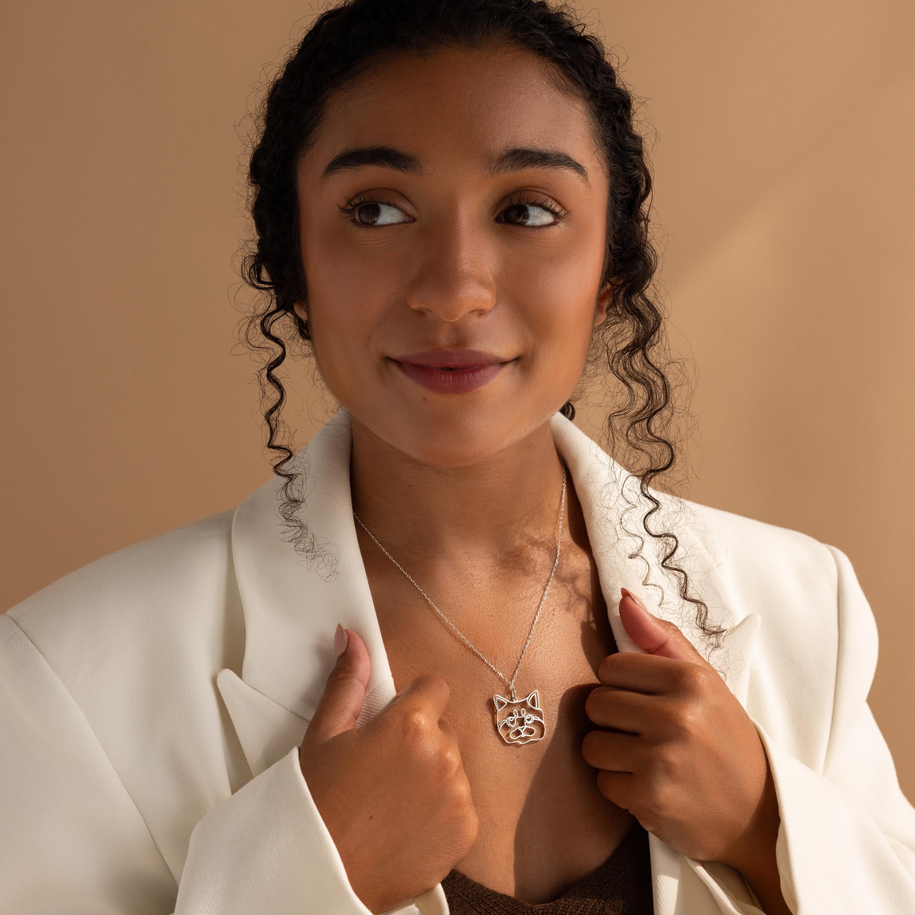 Woman in a white blazer holding a Custom Pet Line Art Necklace shaped like a cat, looking slightly to the side against a neutral background.