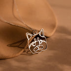A Custom Pet Line Art Necklace in silver, featuring a cat face pendant, displayed on a brown surface with gentle shadows.