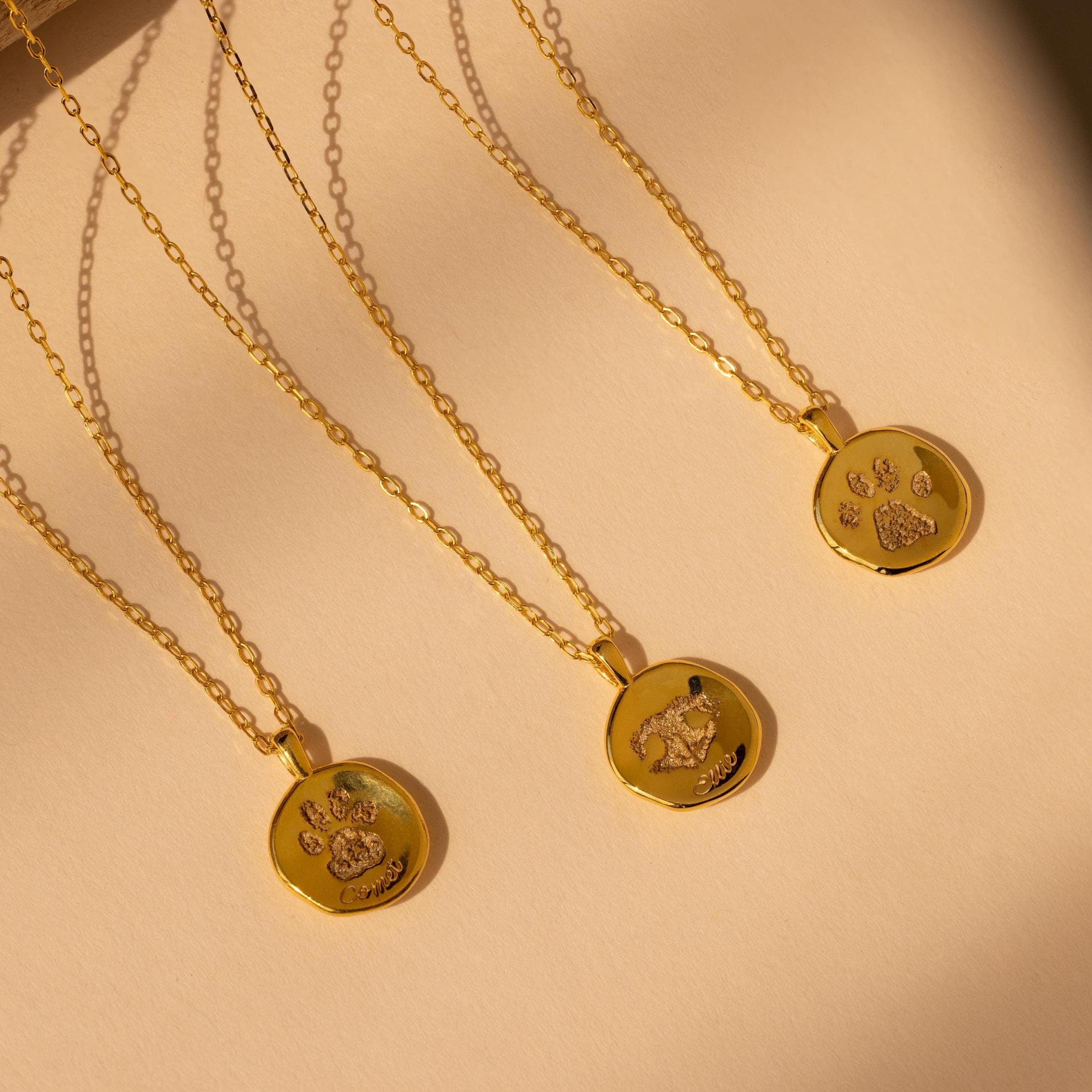 The Paw Print Coin Necklace features a gold round pendant with an animal paw print or dog engraving on a beige background—ideal as a customizable pet necklace or heartfelt pet memorial jewelry.
