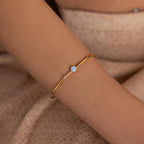 The Opal & Diamond Cuff Bracelet rests elegantly on a person's wrist, set against beige knitted fabric.