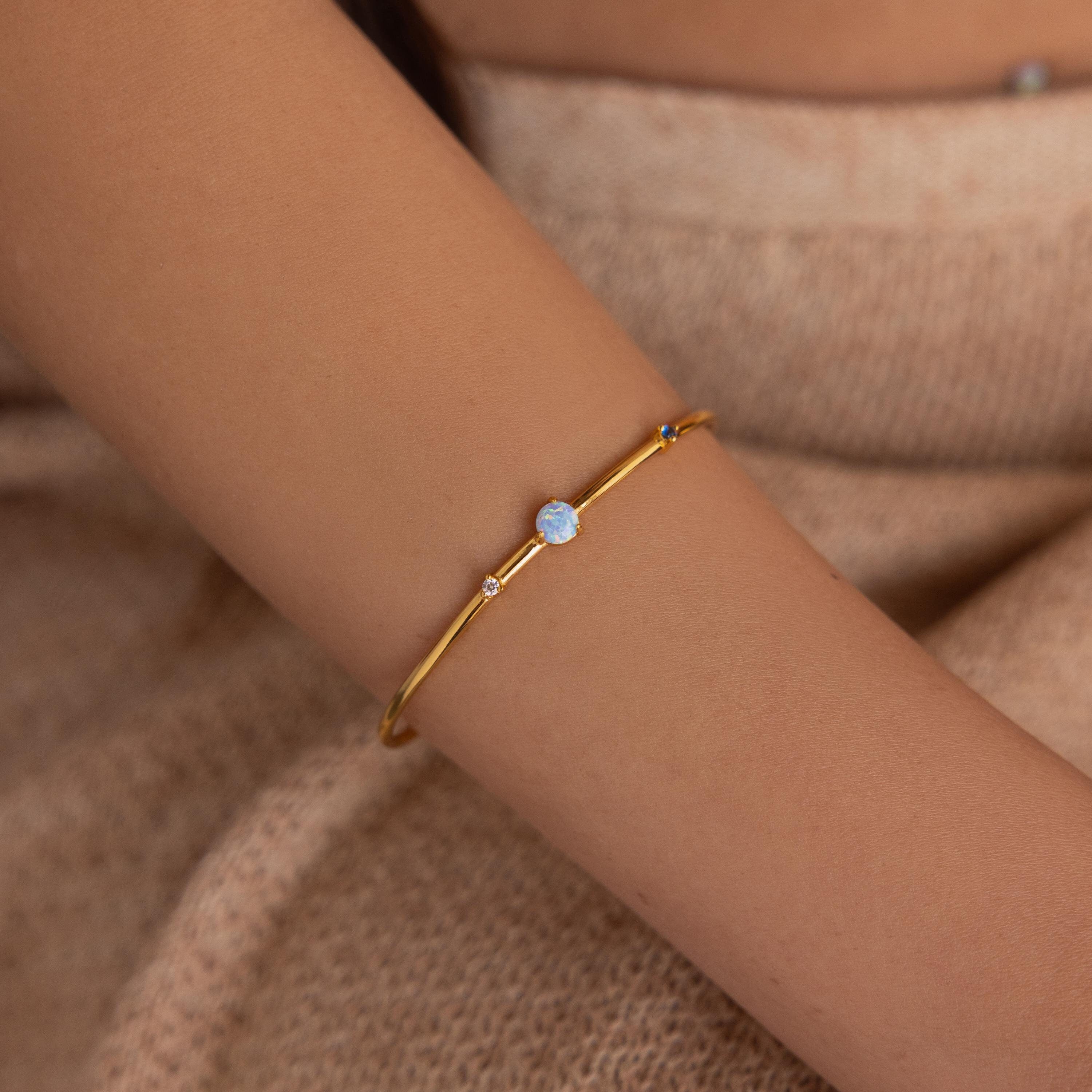 The Opal & Diamond Cuff Bracelet rests elegantly on a person's wrist, set against beige knitted fabric.
