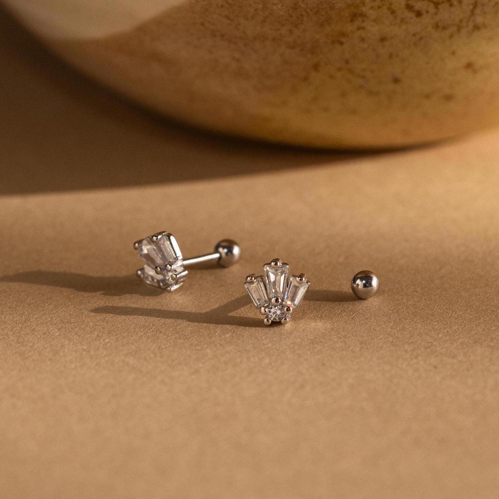 Two Art Deco Studs in silver with clear gemstones shine on a brown surface, their vintage charm highlighted by the softly blurred background.