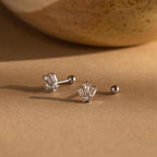 Two Art Deco Studs in silver with clear gemstones shine on a brown surface, their vintage charm highlighted by the softly blurred background.