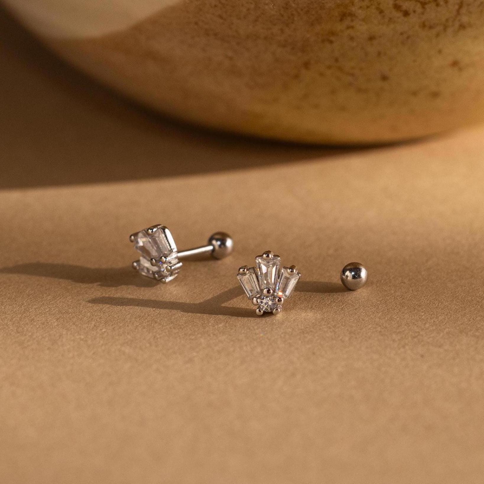 Two Art Deco Studs in silver with clear gemstones shine on a brown surface, their vintage charm highlighted by the softly blurred background.