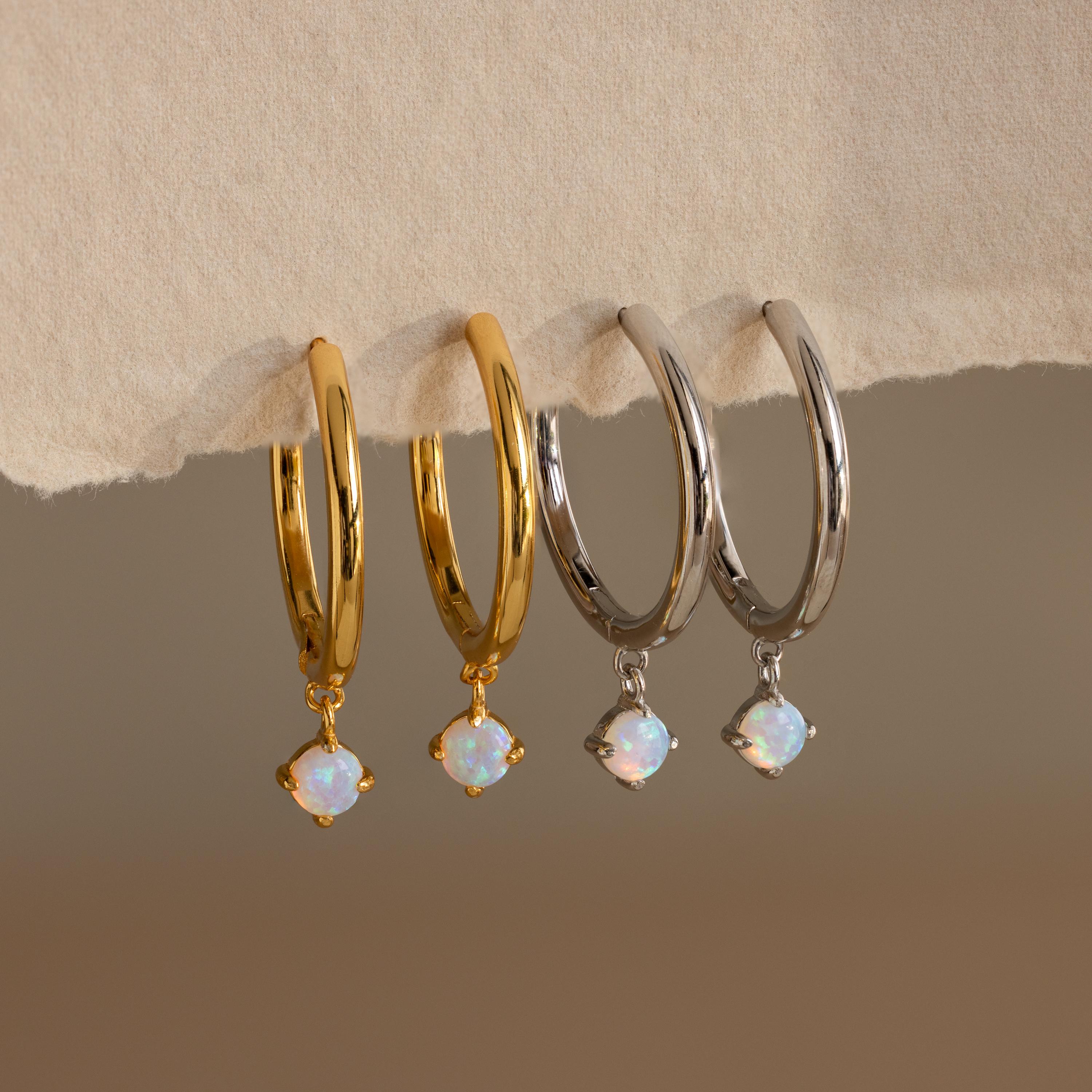 Two pairs of Dainty Opal Drop Huggies—one in gold and one in silver—feature dainty opal drops and rest elegantly on a beige surface.