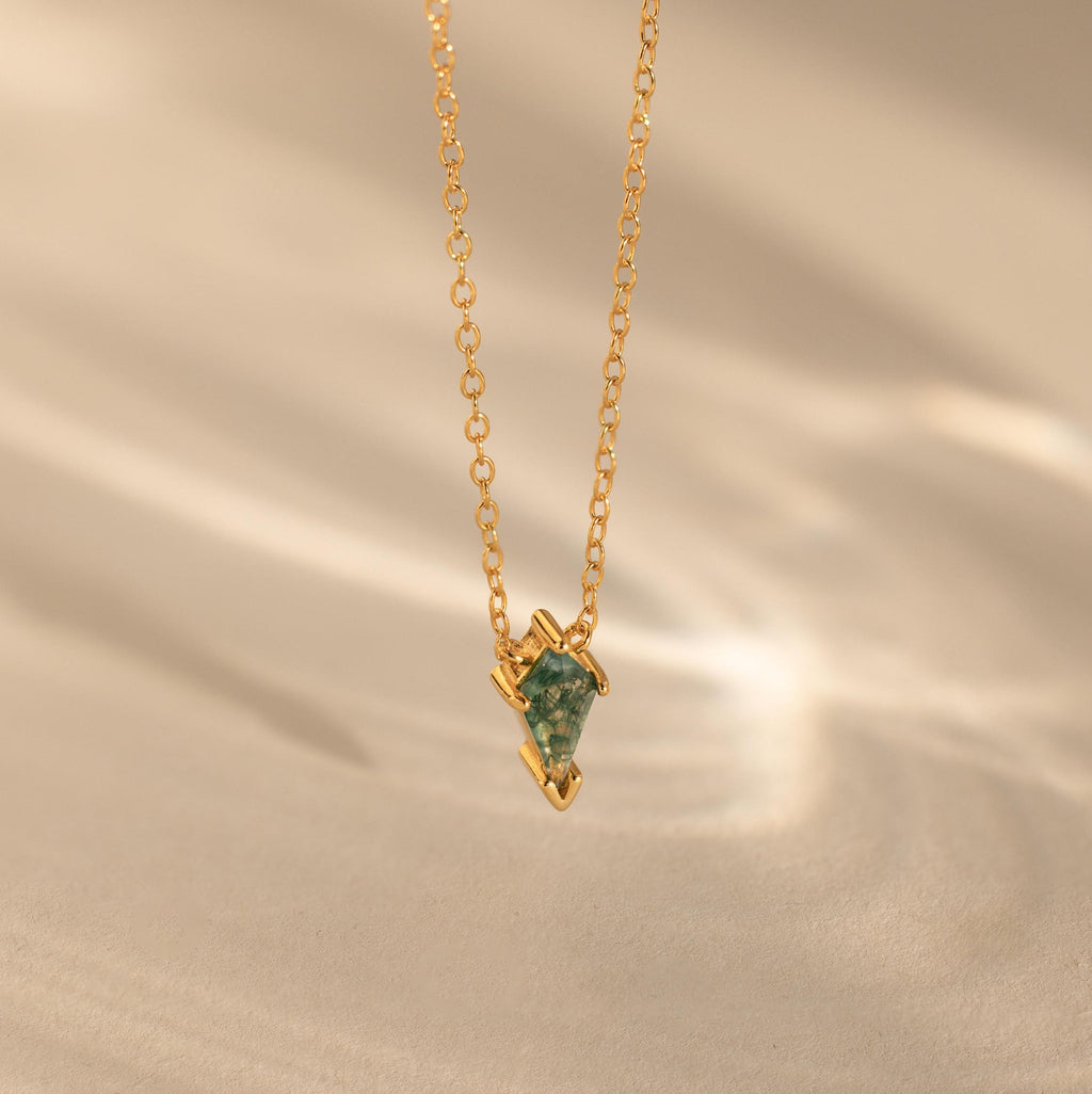 The Agate Art Deco Pendant Necklace features a gold chain and a green geometric moss agate pendant, displayed on a soft beige background for timeless elegance.